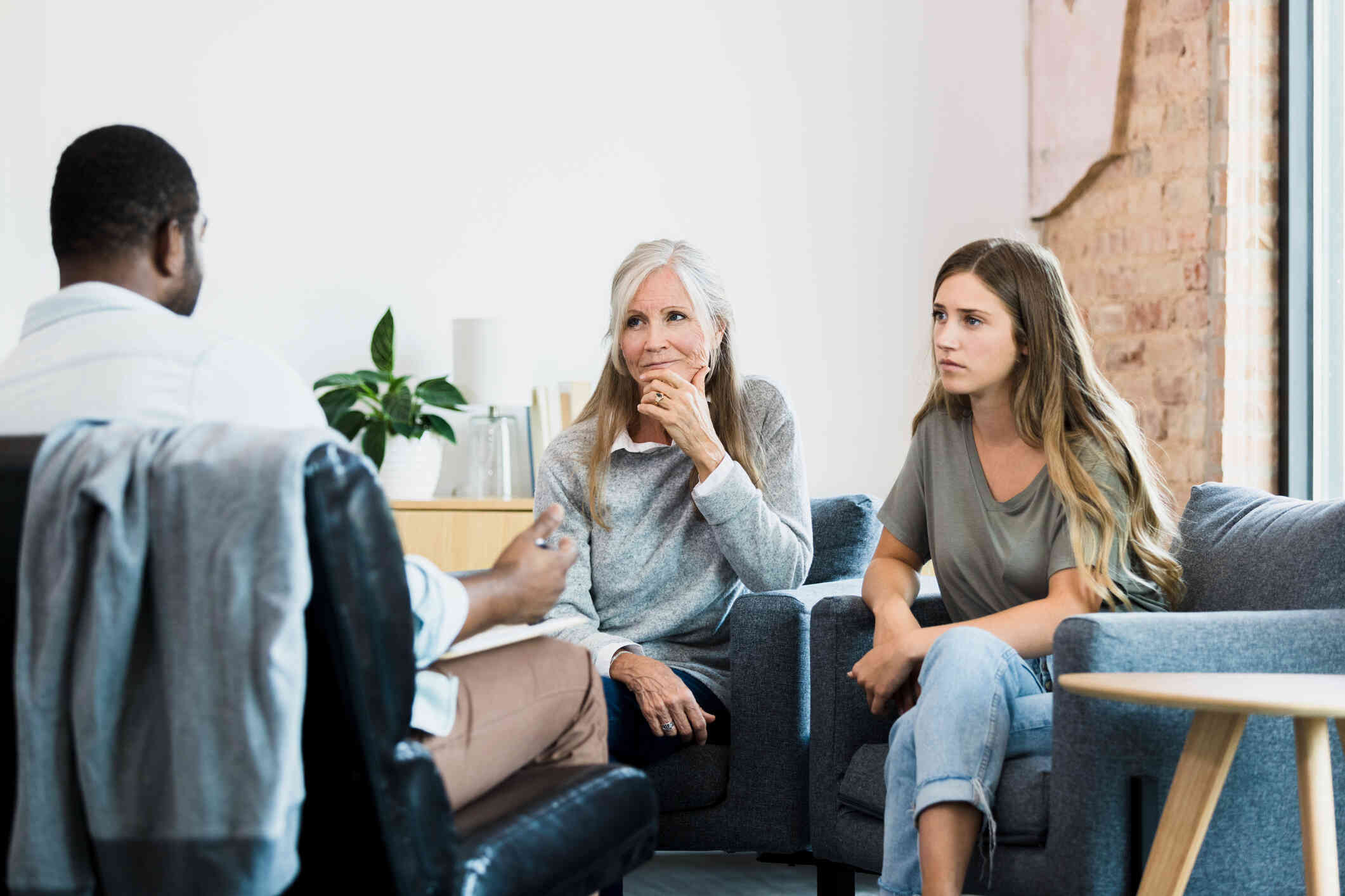 A mother and  teenage daughter sit next to each other during a therapy session with their family therpaist.